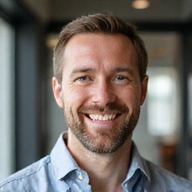 Retrato profesional de un hombre con barba corta y una sonrisa amable, con una camisa de cuello.